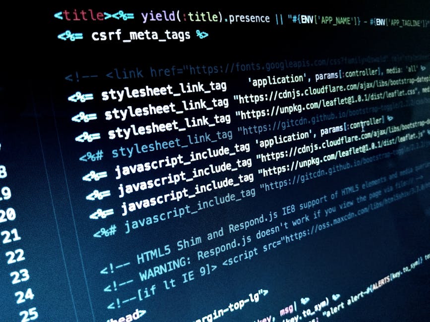 A close-up view of a silver laptop placed on a white desk, displaying lines of colorful programming code on its screen. In front of the laptop, there is a white smartphone positioned face-up, with its